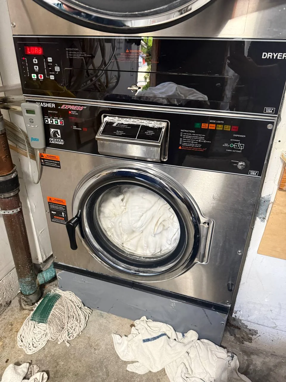 Dexter stacked commercial washer and dryer with towels loaded and a mop on the floor