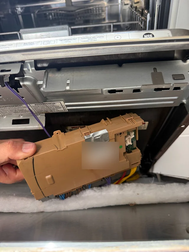 Dishwasher control board held in hand in front of an open dishwasher door