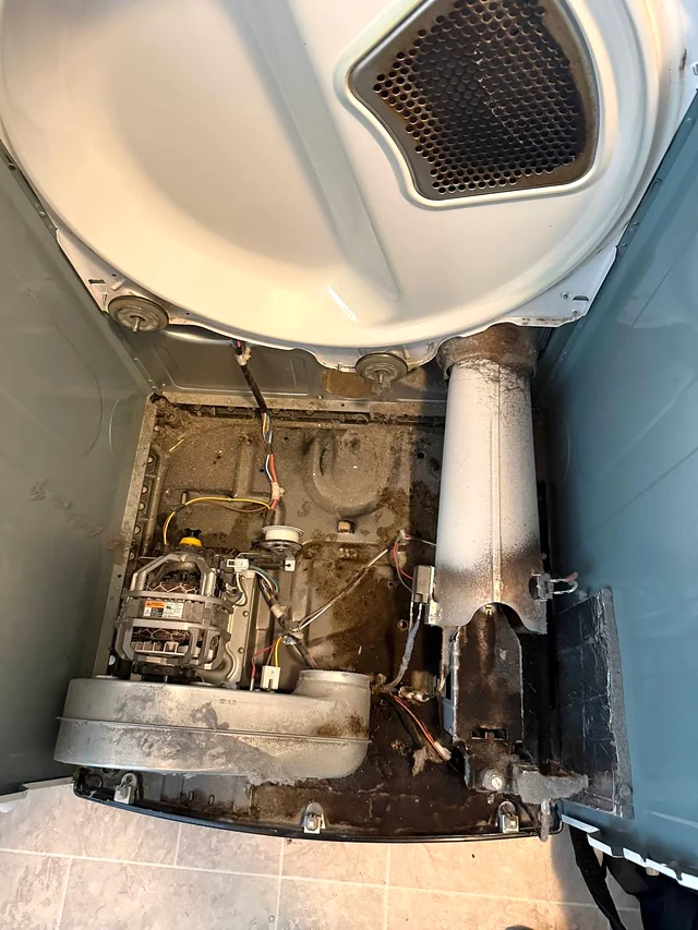 Dryer with the front panel removed showing the motor and a lint-coated vent duct