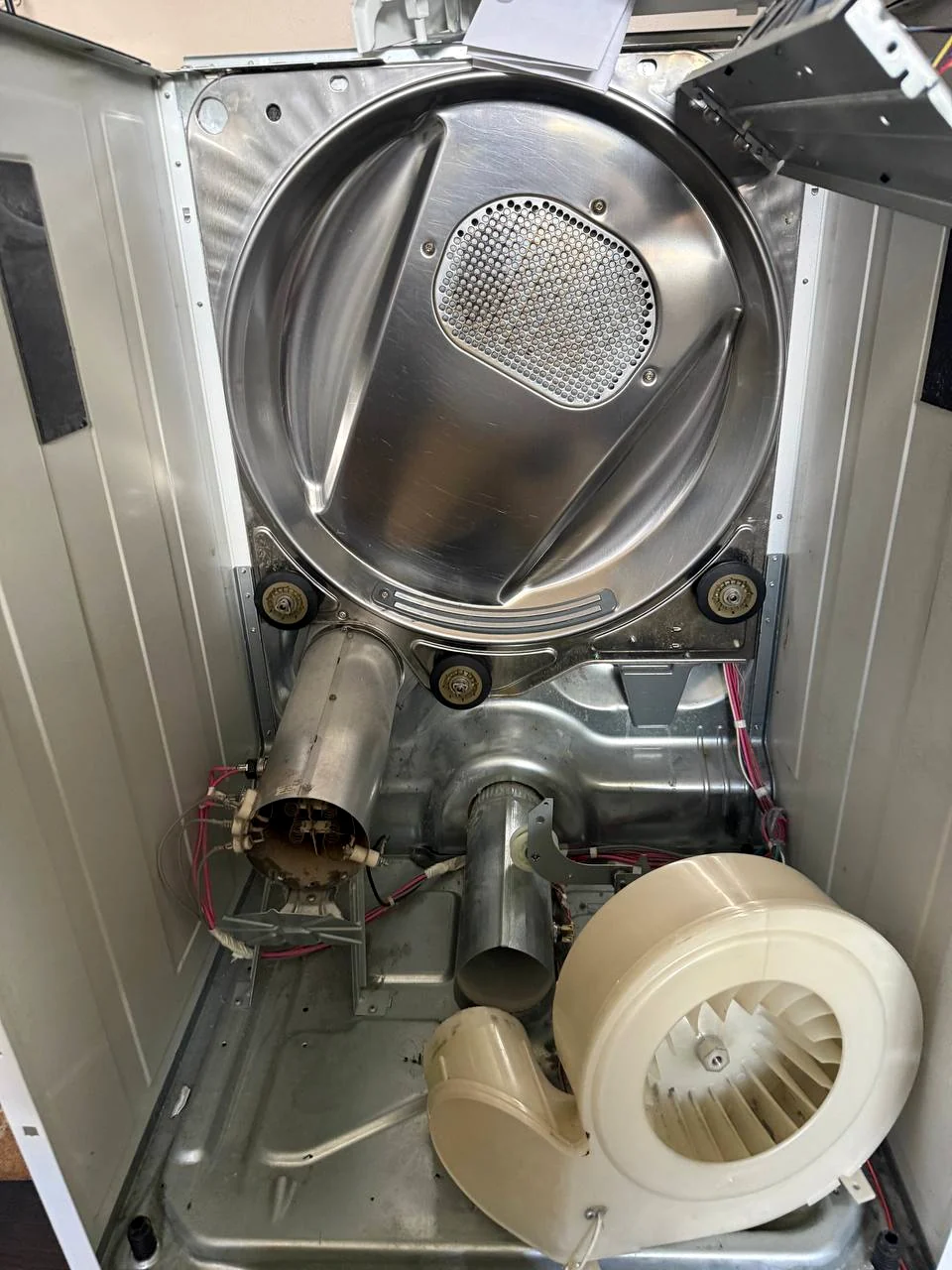 Open dryer cabinet showing the drum, heater housing and blower wheel resting at the base