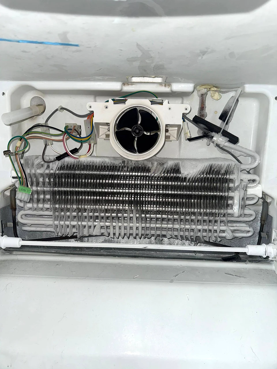 Freezer evaporator coil and fan with wiring exposed behind a removed panel