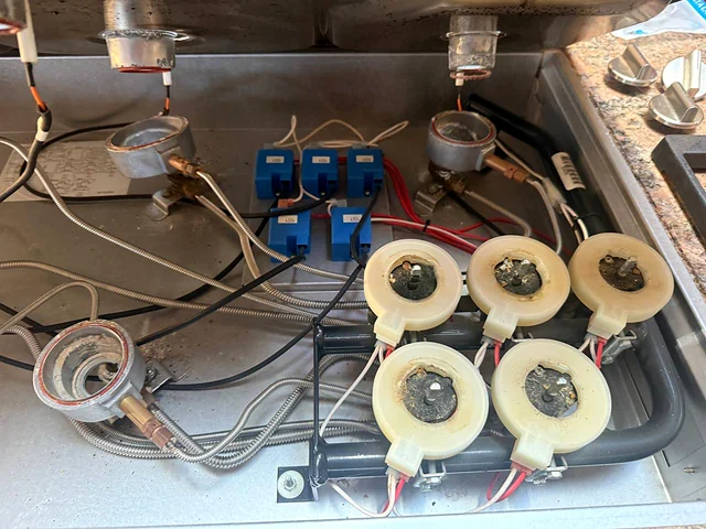 Underside of a gas cooktop showing ignition switches, burner valves and wiring