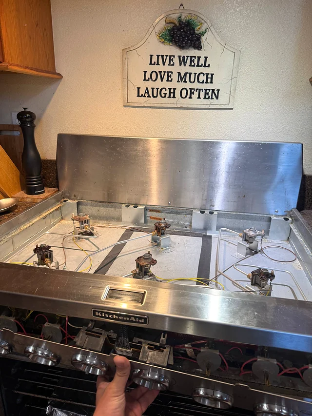 KitchenAid gas cooktop with a burner raised to expose igniter wiring