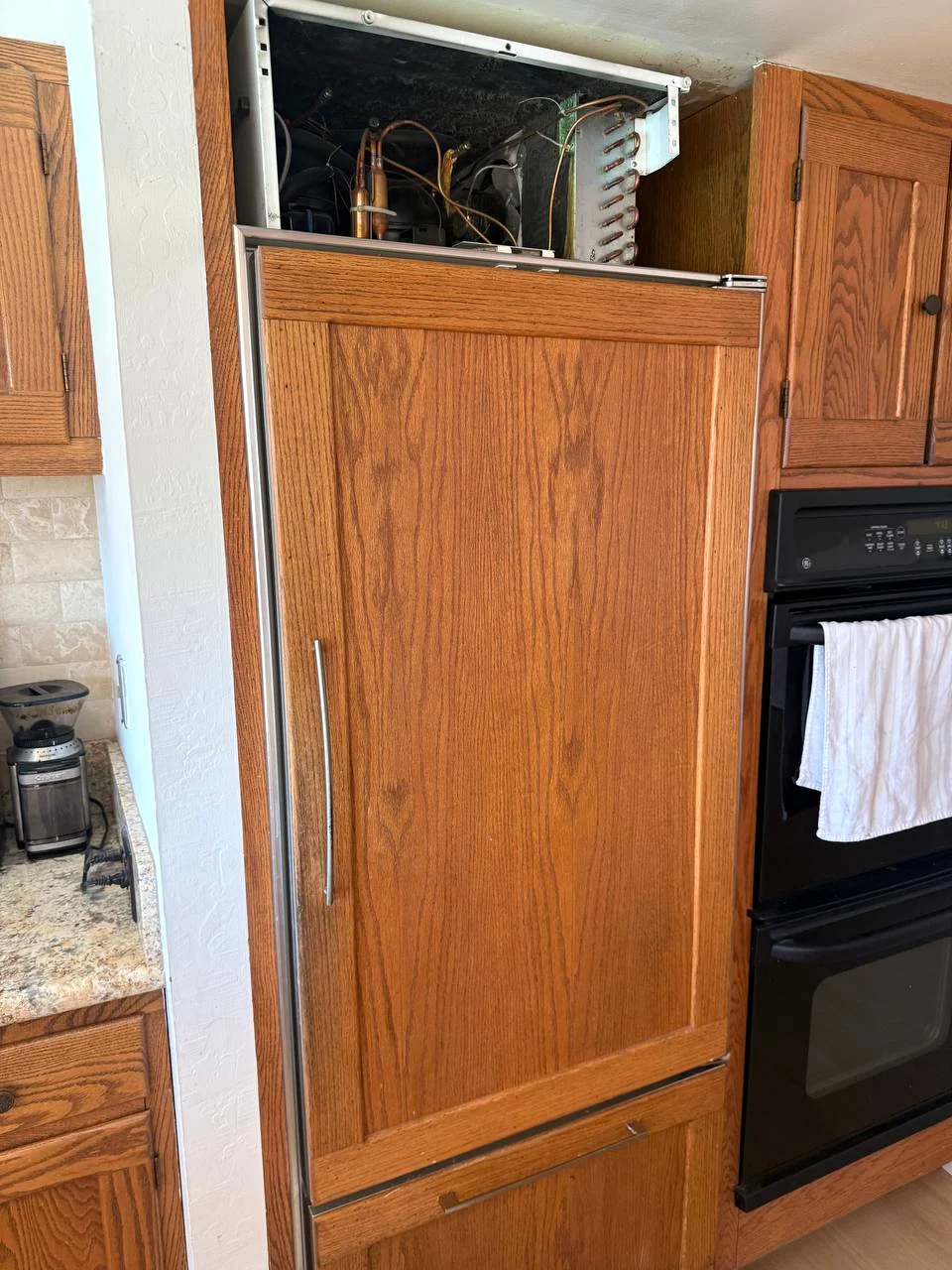 Panel-ready built-in refrigerator with the top grille removed exposing refrigeration components